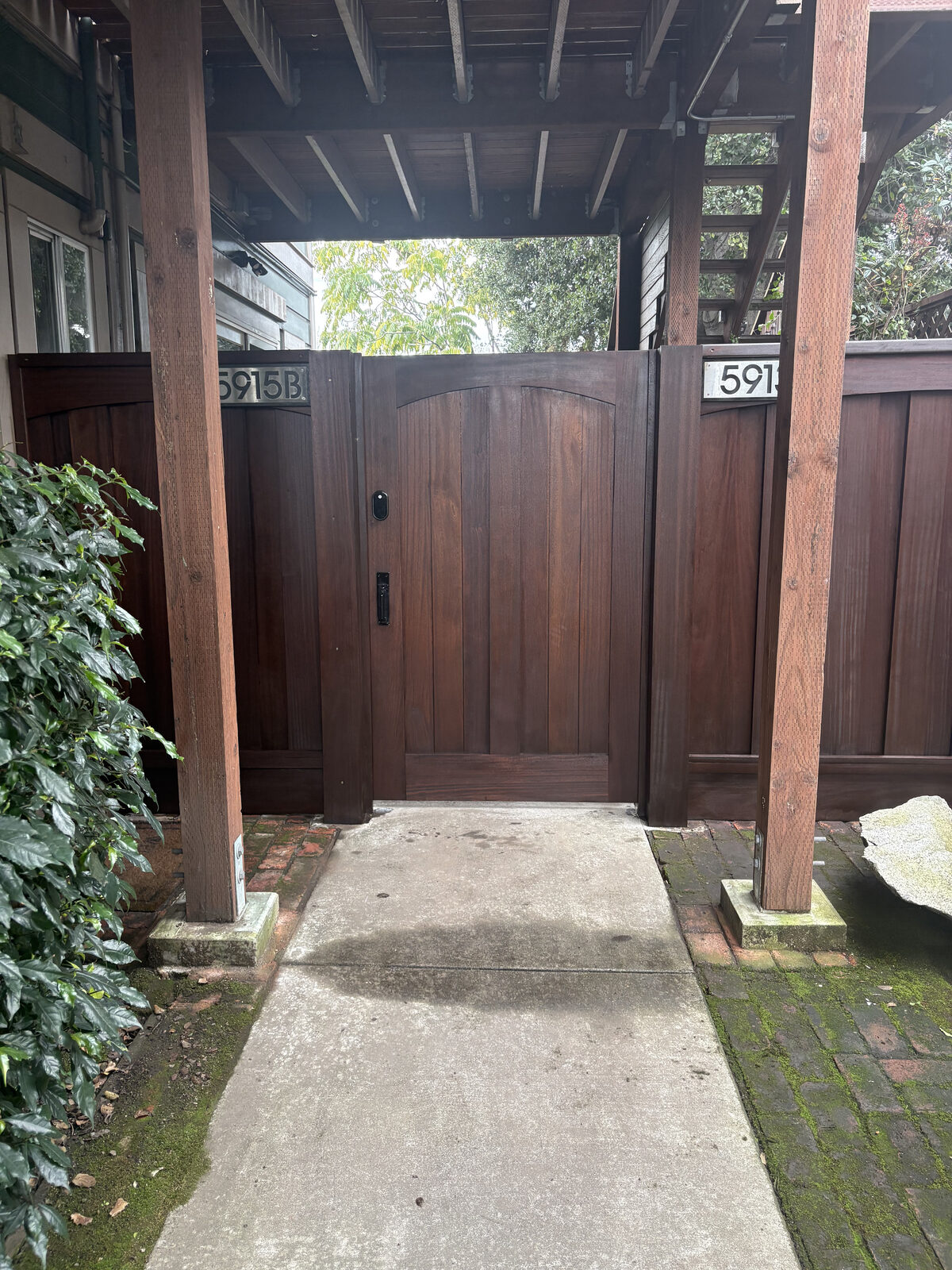 Arched dark-stained mahogany walkway gate with keypad lock between matching fence panels