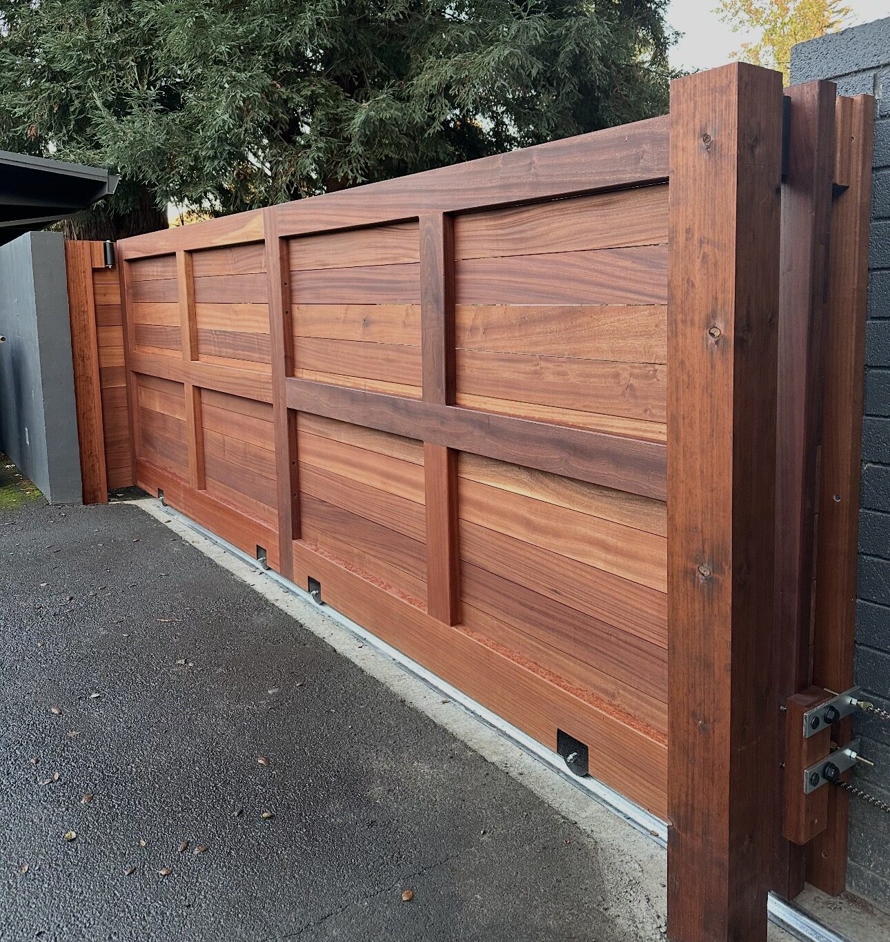 Mahogany horizontal slat sliding driveway gate with cross-rail detail on steel track