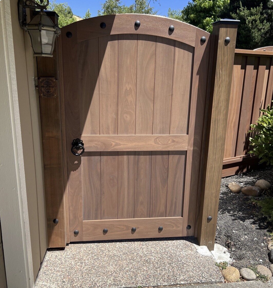 Arched mahogany side gate with iron clavos, ring pull latch and branded Heartwood Gates plaque