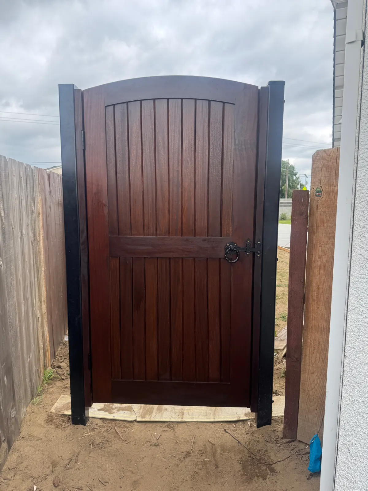 Decorative custom hardwood backyard pool entryway gate with arched top and iron ring latch in Northern California