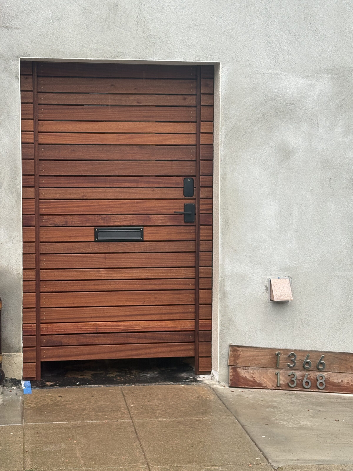 Horizontal slat mahogany entry gate with mail slot and keypad set in stucco wall