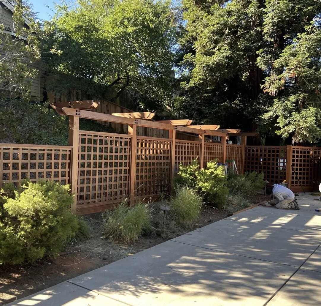 Redwood lattice privacy fence with pagoda-style pergola caps along a garden walkway