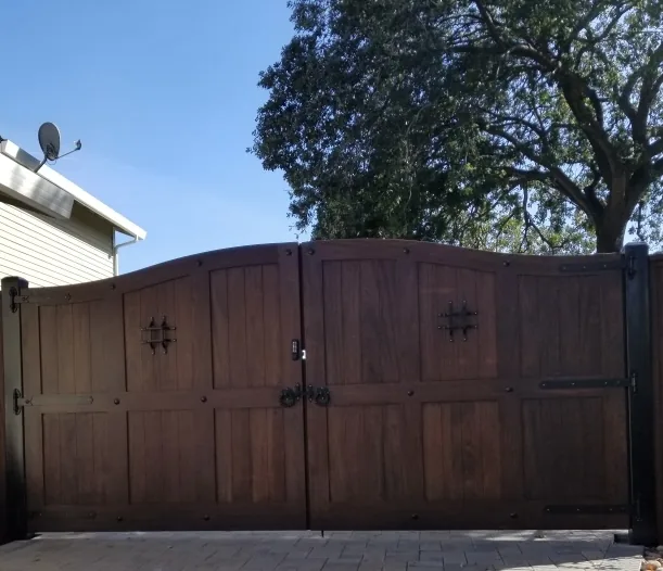 Arched double swing driveway gate in dark stained mahogany with iron strap hardware